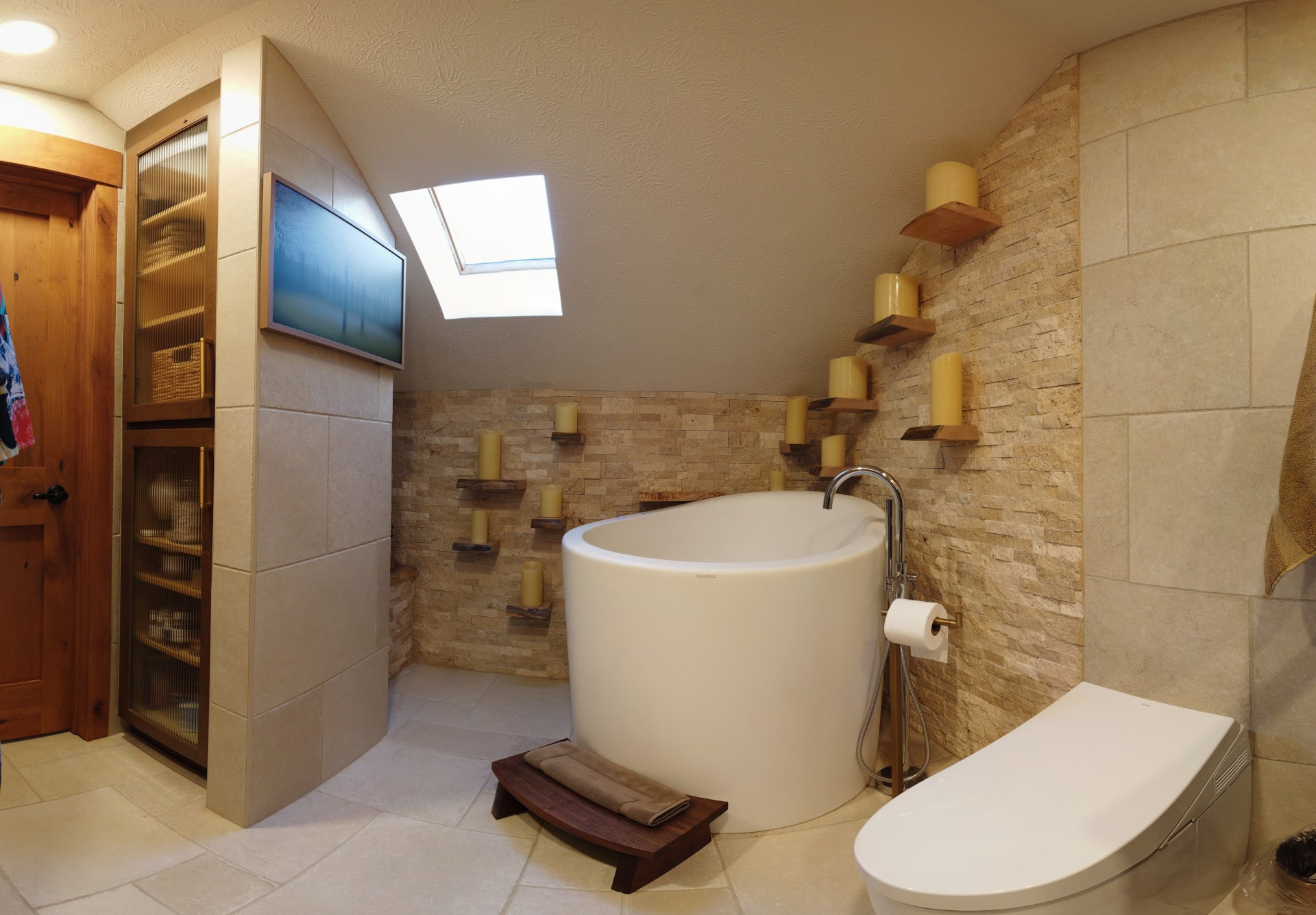 Spa-style bathtub beneath a skylight with stone tile and natural wood shelving