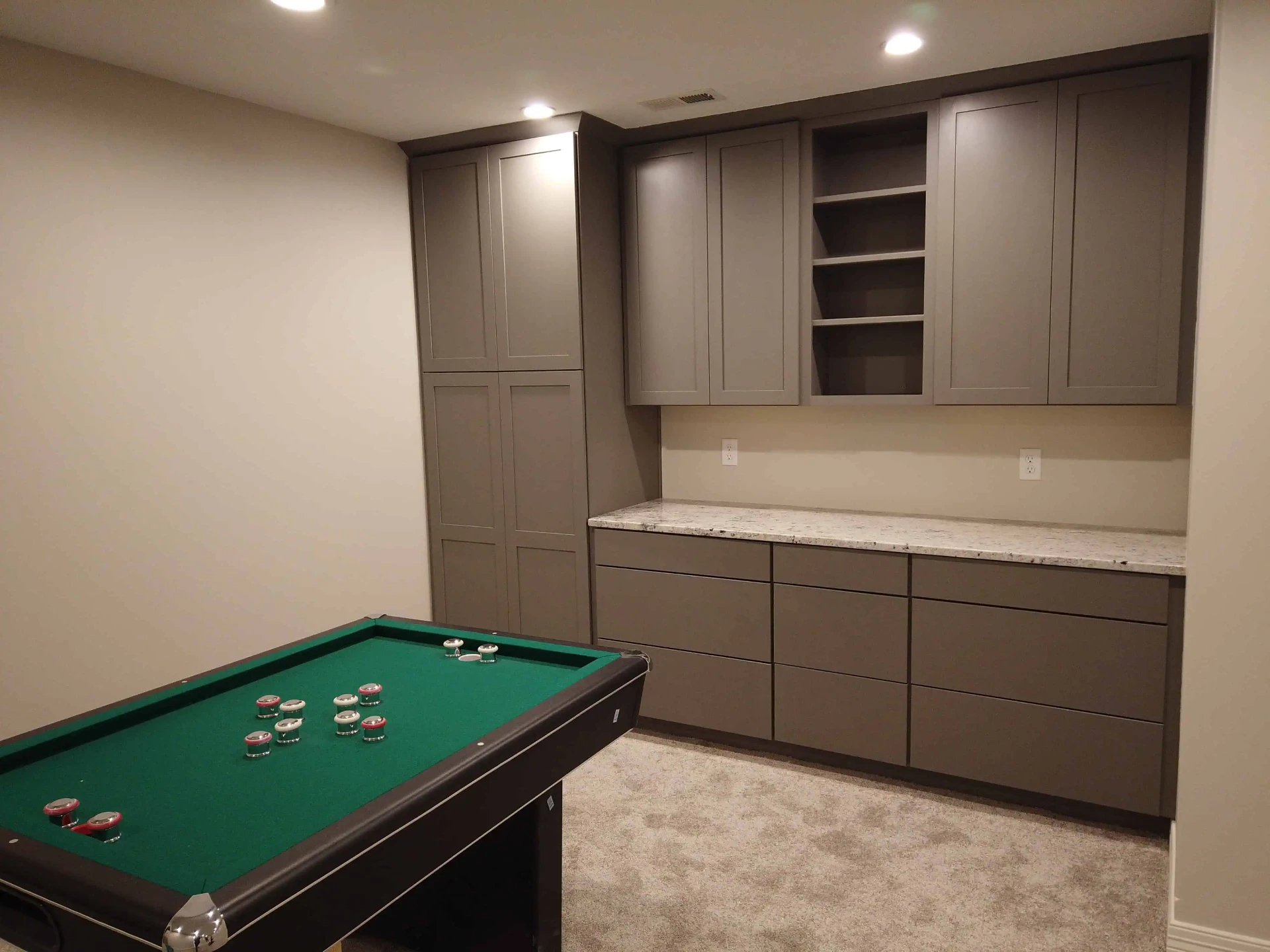 Basement game room with built-in cabinetry and granite counter
