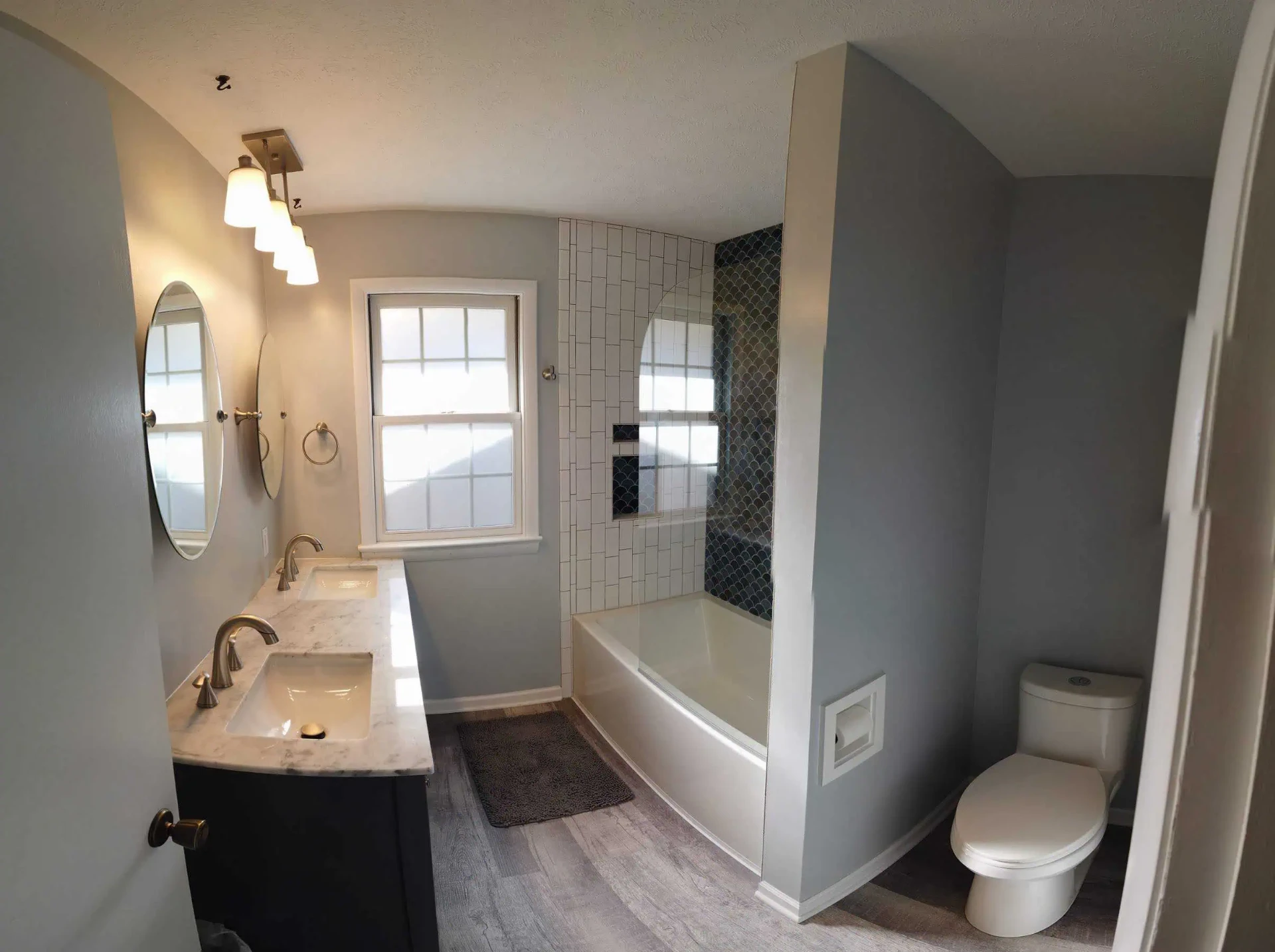 Hall bath with marble double vanity, oval mirrors, and tub shower